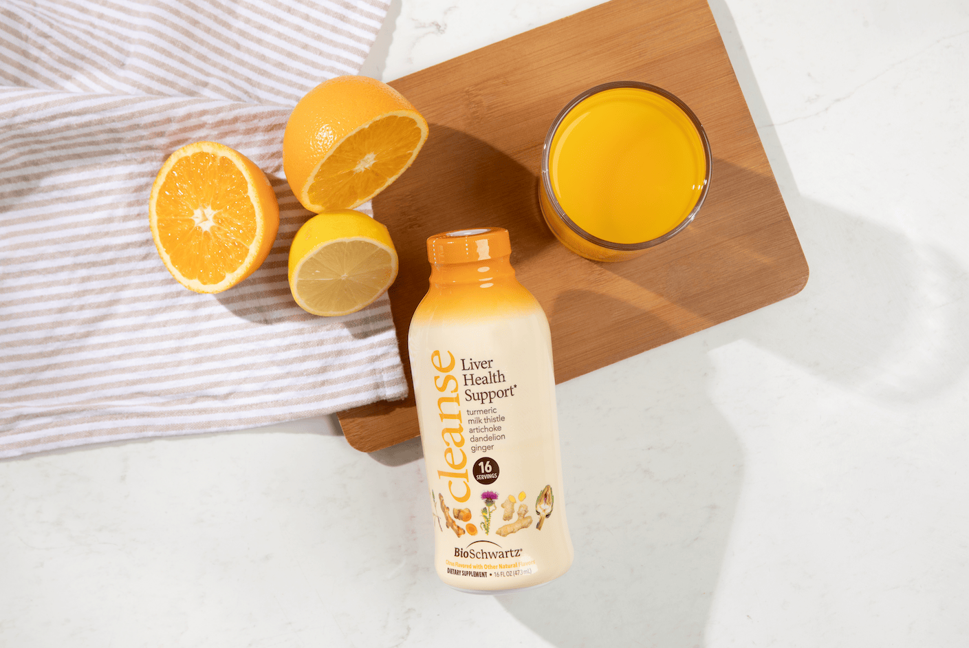 A bottle of Cleanse Liver Health Support juice supplement placed on a wooden cutting board next to a glass, sliced oranges, a lemon, and a striped cloth on a white marble surface.